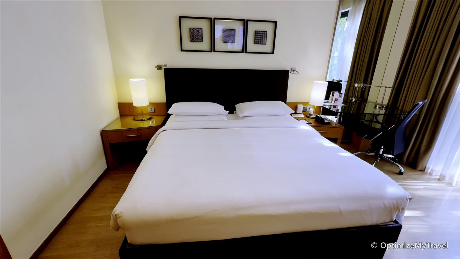 Deluxe Balcony Room with a large bed, bedside tables, work desk, and glass doors