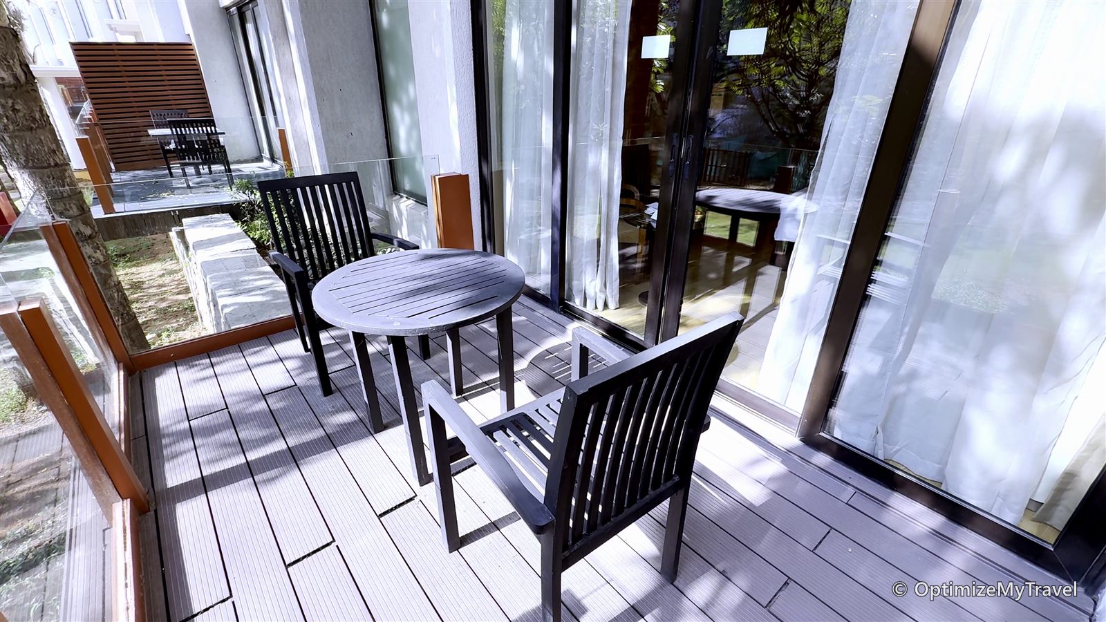 Side view of the balcony showing two chairs, a table, glass railing, and room entrance